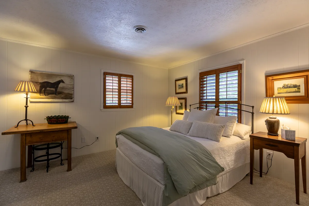 A serene bedroom featuring a comfortable bed with a green throw, soft bedside lighting, framed artwork, and wooden furniture. The space feels inviting and peaceful, perfect for restful sleep and morning relaxation.