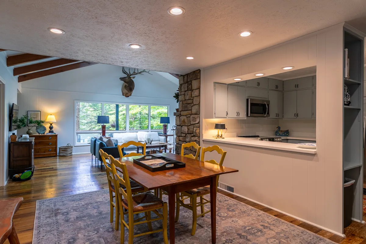 An inviting dining area with a large table surrounded by cheerful yellow chairs, a striking stone feature wall, expansive windows flooding the space with natural light, and subtle antler decor that nods to the mountain setting. The space feels lively and perfect for shared family moments.