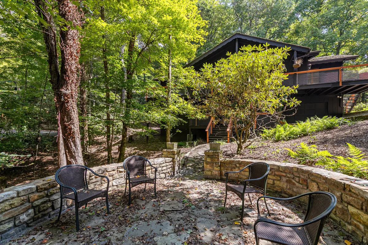 An exterior view highlighting a modern house structure set amidst lush greenery and a stone seating area. The surroundings are peaceful and secluded, conveying both natural beauty and a sense of privacy.