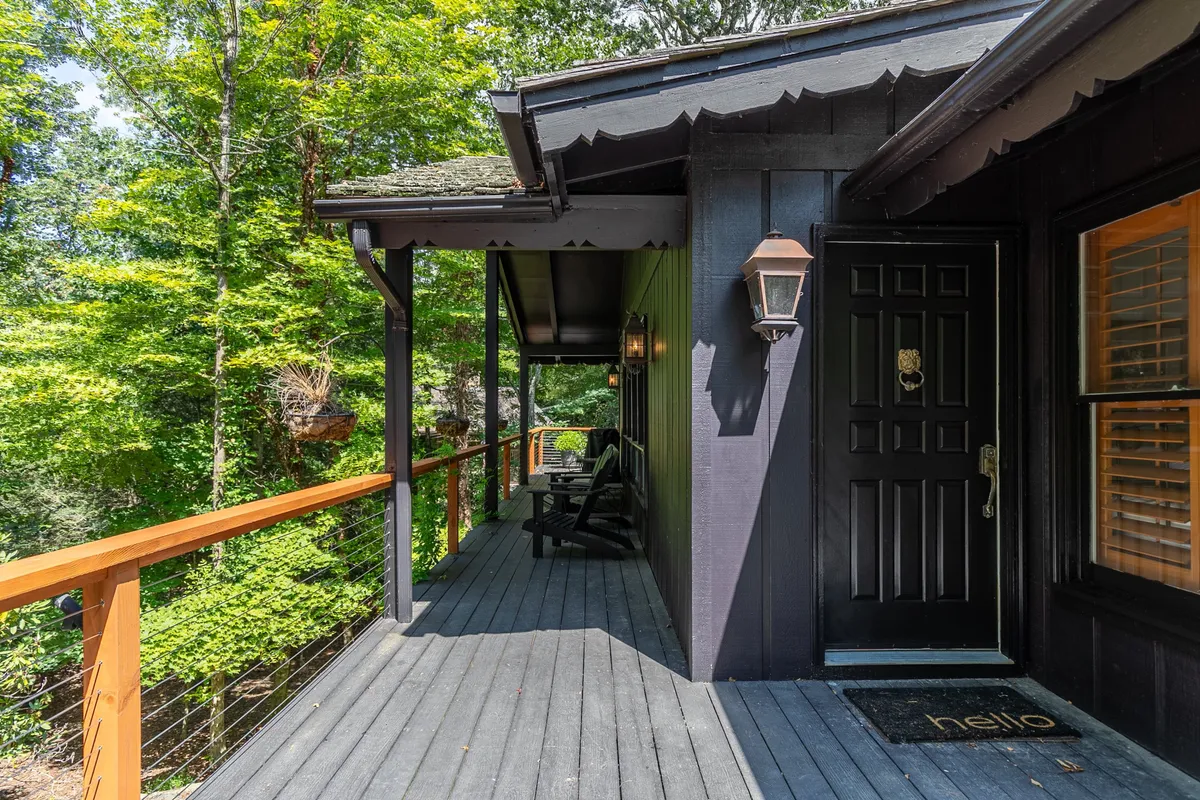 This exterior image shows the welcoming front door of Elk Watch, flanked by a lantern light, inviting deck railing, and classic rocking chairs. The porch is surrounded by natural elements, offering a serene and private entrance experience.