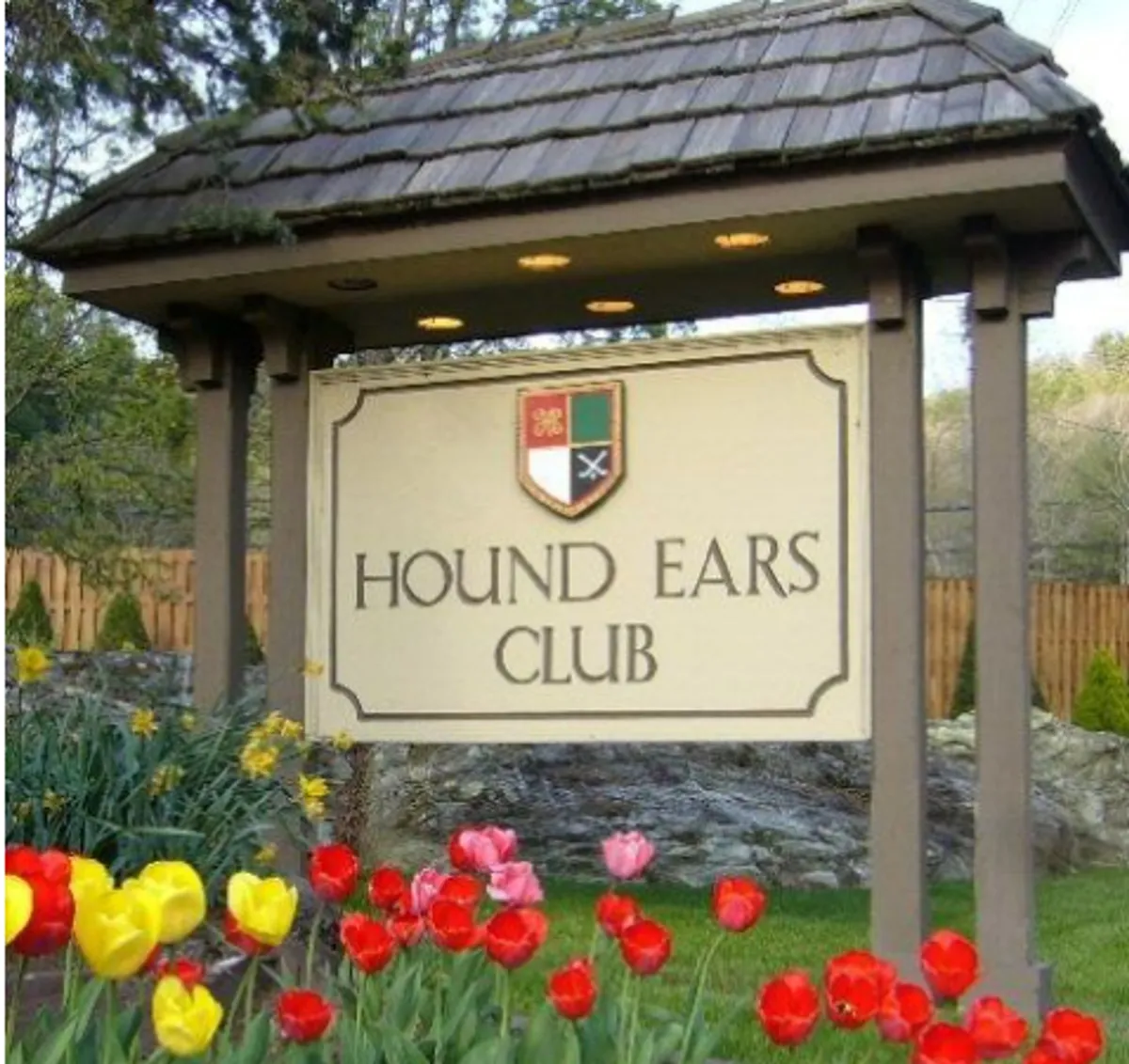 The image captures the signage for Hound Ears Club surrounded by vibrant tulips, with a clear sense of arrival and community pride. The cheerful landscaping and prominent signage immediately signal exclusivity and a well-maintained environment.