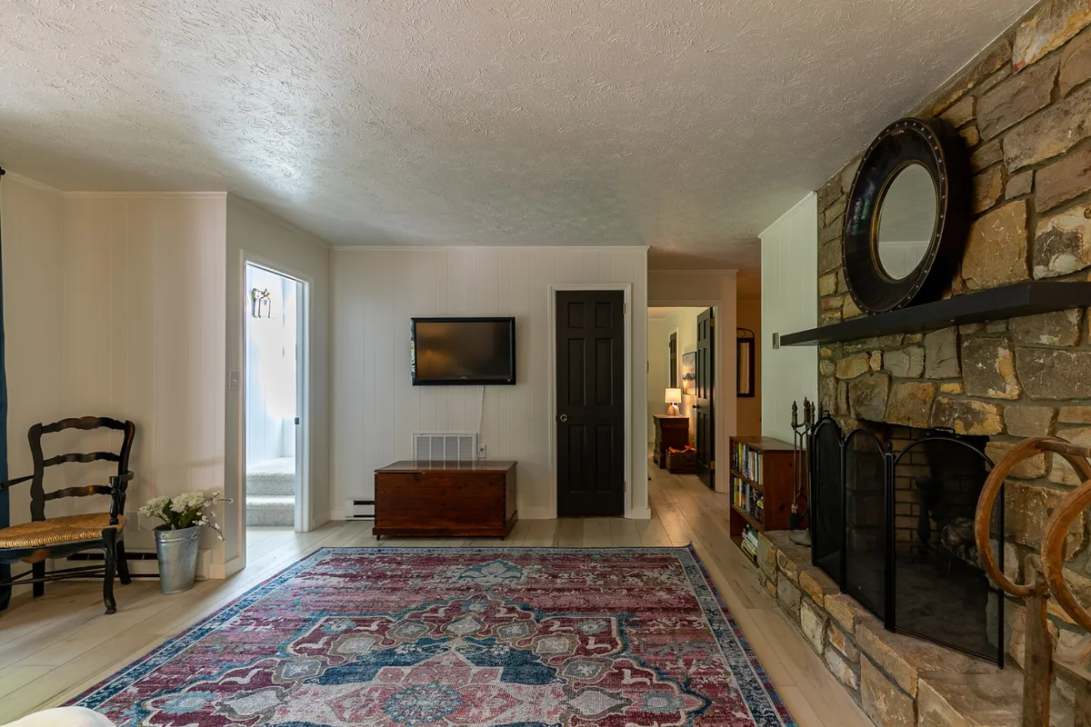 This inviting living area features a cozy fireplace, rug, television, and a visible doorway that leads outside. The room is arranged for relaxation and gatherings, and the doorway visually links the interior to the deck or yard beyond, implying convenient access for both guests and pets.